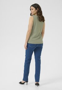 Haut sans manches vert olive et jeans bleus. Le haut a une texture lisse ; les jeans sont coupés droit avec un design classique. Des talons noirs complètent la tenue.