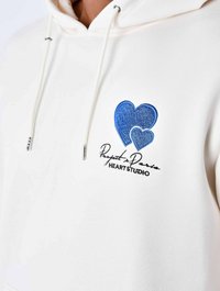 Sweatshirt à capuche blanche avec des cœurs brodés bleus et le texte "Project D." Comprend des cordons et une texture douce.