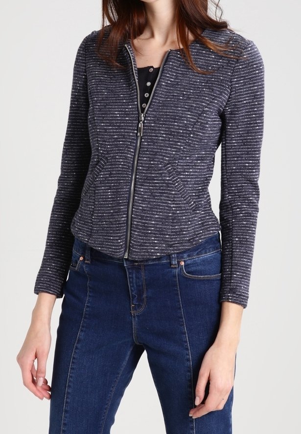 Donkerblauwe jas met ritssluiting met licht gevlekt patroon, lange mouwen, gestructureerde stof en een getailleerde pasvorm, gecombineerd met donkerblauwe spijkerbroeken.