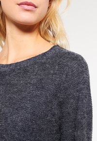 Dark gray wool sweater with a round neckline, textured knit, and soft appearance. Displays a relaxed fit and subtle, natural sheen.