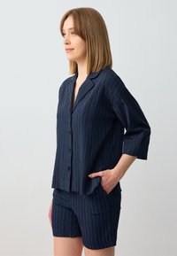 Set di pigiama a righe blu navy composto da una camicia con bottoni, colletto e maniche a tre quarti, abbinata a pantaloni corti coordinati. Tessuto morbido e testurizzato.