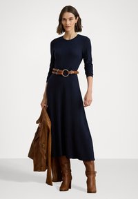 Marineblå strikket kjole med lange ermer, belte med brun lær og en gullsirkel-spenne; kombinert med brune thigh-high støvler med hæl.