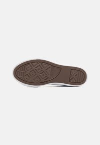 Semelle de sneaker avec un motif en caoutchouc brun détaillé, présentant des éléments de grip texturés et une paroi latérale blanche. Forme arrondie avec un matériau flexible.