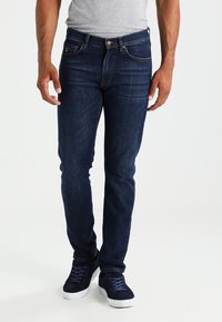 Pantalones vaqueros de denim azul oscuro con un corte ajustado, que presentan un desgaste sutil, diseño de cinco bolsillos, costuras en contraste y cierre de botón.