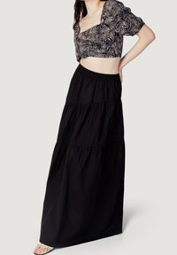 Schwarzer, gestufter Maxirock mit elastischem Taillenbund, kombiniert mit einem kurzärmeligen Cropped-Top mit einem monochromen Blattmuster und kurzen Puffärmeln.