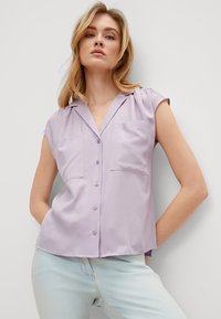 Lavender short-sleeve shirt with a notched collar, two front pockets, and button closure. Smooth fabric with a subtle sheen.