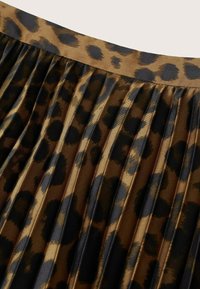 Jupe plissée en tissu brillant avec un motif léopard marron et noir et une ceinture assortie.