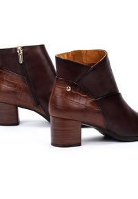 Bottines en cuir marron avec un dos embossé crocodile, bout rond et détail de fermeture éclair dorée. Talon moyen et texture lisse.