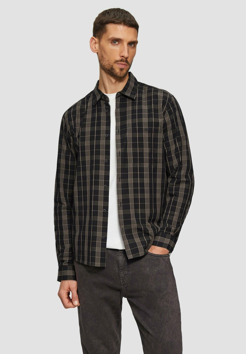 Chemise à carreaux noire et beige à bouton, avec une poche poitrine et des manches longues, assortie à un pantalon gris foncé. Texture de tissu lisse.