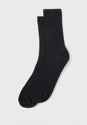 Para czarnych prążkowanych skarpet sięgających do połowy łydki, ułożonych płasko, z wzmocnionym obszarem pięty i palców, na białym tle.