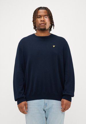 Pull en maille bleu marine avec un col rond et des manches longues. Présente un petit logo jaune sur la poitrine. Texture douce et coupe décontractée.