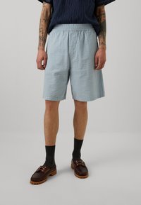 Pantaloni corti azzurri testurizzati con vita elastica, design fino al ginocchio, abbinati a calzini scuri e mocassini marroni.