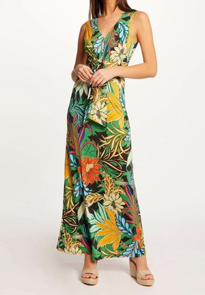 Długa sukienka bez rękawów z dekoltem w serek, w wielokolorowy tropikalny kwiatowy wzór, z paskiem w talii, noszona z beżowymi sandałami na koturnie.