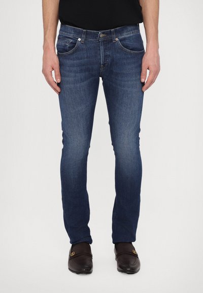 Jeans din denim de culoare albastru închis, cu croi slim, design cu cinci buzunare și detalii de cusătură vizibile. Purtați cu pantofi maro.