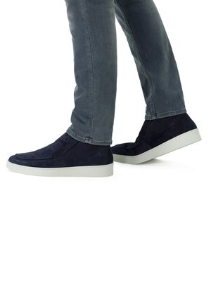 Navy suède instappers met een witte rubberen zool, met een gladde textuur en eenvoudig ontwerp, gedragen met lichtgrijze jeans.