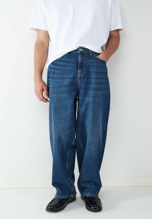 Leichte blaue Jeanshosen mit lockerer Passform, klassischem Fünf-Taschen-Design und Kontrastnähten. Kombiniert mit einem schlichten weißen T-Shirt.