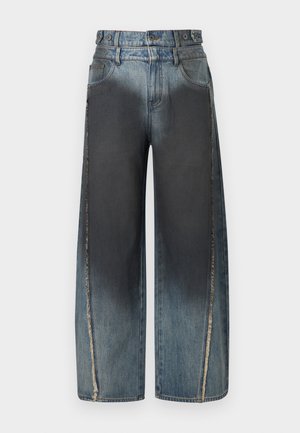 Jean bleu à jambes larges avec des taches délavées plus foncées sur le devant et des coutures verticales effilochées sur les jambes extérieures.