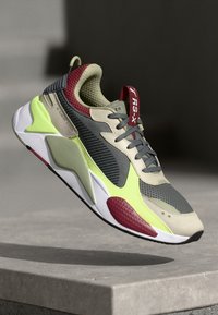 Gray and lime green sports shoe featuring mesh and synthetic materials, prominent padded tongue, and red accents on the heel and tongue.