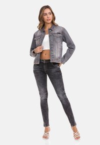 Jeansjacke in verblasstem Grau mit zwei Brusttaschen, orangefarbener Naht und cropped Design. Kombiniert mit schwarzen Skinny Jeans und weißen Sandalen.