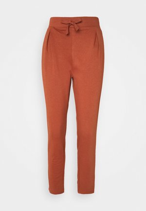 Pantalon fuselé de couleur rouille en tissu doux et texturé, avec une taille à cordon de serrage et des plis avant pour plus de détails.