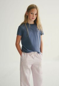 Námořnické bavlněné tričko s krátkým rukávem, spárované se světle růžovými kalhotami s vertikálními pruhy v zelené a modré barvě. Casual střih, včetně kapes.