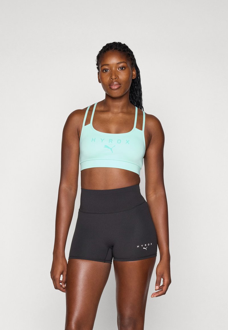 Soutien-gorge de sport vert menthe avec des fines bretelles et le texte "HYROX", associé à un short noir taille haute avec un petit logo. Texture lisse.