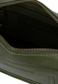 Borsa in pelle verde scuro aperta con cerniera visibile e foderatura in tessuto interna, che mostra il compartimento principale vuoto.