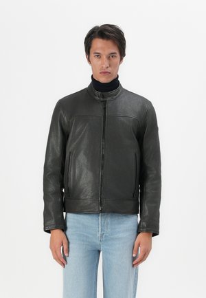 Black leather jacket with a round collar, front zip, and two side pockets. Textured finish; paired with light blue jeans.