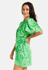 Green dress featuring a swirling pattern, short sleeves, a cinched waist with a tied detail, and a smooth, lightweight fabric.
