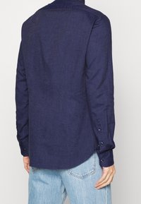 Camicia a maniche lunghe blu navy in tessuto testurizzato, con orlo curvo e polsini abbottonati. La vista posteriore mostra un design di colletto classico.