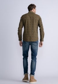 Langsleeve bruine shirt met een groen en oranje abstract patroon, gecombineerd met blauwe jeans en beige laarzen. Zichtbare stiksels en knoopdetails.