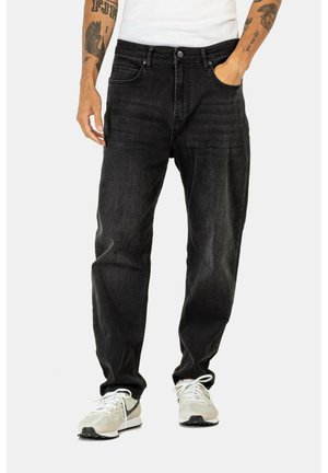 Schwarze Jeans aus Denim mit geradem Schnitt, Fünf-Taschen-Design, sichtbaren Nähten und einer leicht ausgeblichenen Textur, kombiniert mit hellen Sneakers.