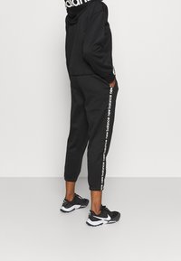 Svart sweatshirt och joggers i mjukt tyg. Huvtröja med logotyp, joggers har vit text på sidan. Svarta träningsskor.