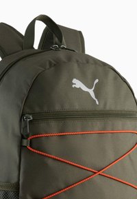 Olivgrön ryggsäck i texturerad tyg med en vit Puma-logotyp, dragkedjeförsedd framficka och orangea gummisnoddar i accenter.