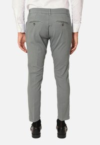 Pantaloni chino grigio chiaro con una vestibilità slim, tasche posteriori con chiusura a bottone, abbinati a scarpe nere e calzini scuri.