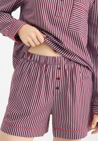 Set di pigiama a righe rosse e bianche, composto da una maglia con bottoni e tasca sul petto e pantaloni corti abbinati con vita elastica e bottoni.