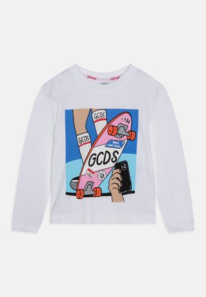 White long-sleeve shirt featuring colorful graphic with a skateboard and hands holding a phone. Bold text "GCDS" prominent in the design.