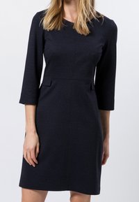 Marineblaues Shiftkleid mit drei Viertelärmeln, Rundhalsausschnitt, zwei seitlichen Taschen und subtiler Textur.