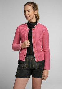 Rosa gestrickte Strickjacke mit gerippter Textur, runder Halslinie und orangen Knöpfen. Kombiniert mit schwarzen Leder-Shorts mit gestickten Details.