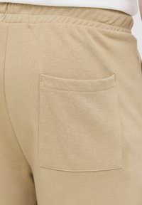 Beige cotton shorts featuring an elastic waistband and a rear patch pocket with a clean finish. The fabric has a smooth texture.