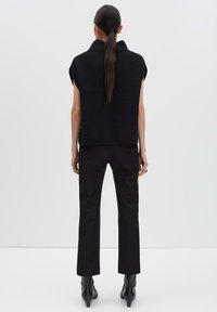 Haut sans manches en maille côtelée noire avec un col montant, associé à un pantalon noir ajusté et des bottines pointues, vu de dos.