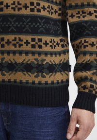 Kootud sviiter, millel on musta, roheline ja pruunika mustriga geomeetrilised kujundid. Mustad ribitud varrukad ja ääred. Valmistatud pehmest tekstiilmaterjalist.