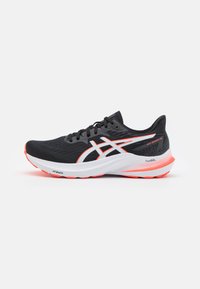 Zapatilla deportiva negra con detalles en blanco y naranja neón, parte superior de malla, suela acolchada y talón reforzado. Presenta cordones y detalle del logo.