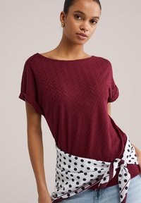 Bordo strukturen zgornji del z širokim izrezom in zavihanimi rokavi, kombiniran z belo obleko na točke, ki se zaveže v pasu, čez svetlo modre kavbojke.