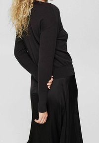 Czarny sweter dzianinowy z okrągłym dekoltem, ściągaczami przy mankietach i w pasie, w zestawieniu z jedwabną czarną spódnicą, zaprezentowany z boku.