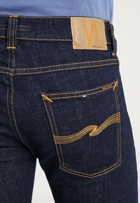 Mörkblå denimjeans med orange sömmar och en läderetikett i midjan. Har en rundad fickdesign.