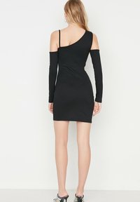 Vestido negro ajustado con mangas largas y un corte en un hombro, con textura acanalada y una silueta entallada.