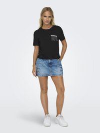 Zwarte T-shirt met korte mouwen en gestreepte pocketdetails, gecombineerd met een lichte denimrok met patch pockets, en witte sneakers.