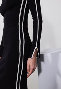 Abito in maglia nero con strisce verticali bianche sulle maniche. Presenta una silhouette aderente, un tessuto testurizzato e uno spacco all'orlo delle maniche.