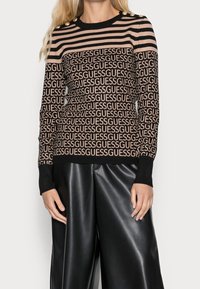 Maglione a maglia con righe orizzontali nere e beige e motivo logo "GUESS"; decorato con bottoni dorati sulla spalla.